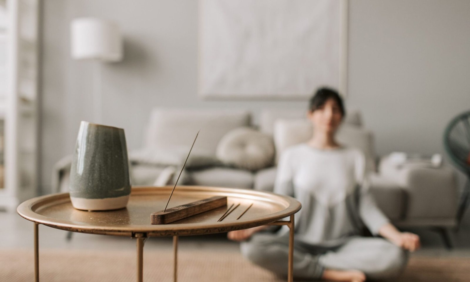 Persona meditando en casa sentada en el suelo, con incienso encendido sobre una mesa en primer plano, en un ambiente tranquilo y minimalista, durante su meditación online.